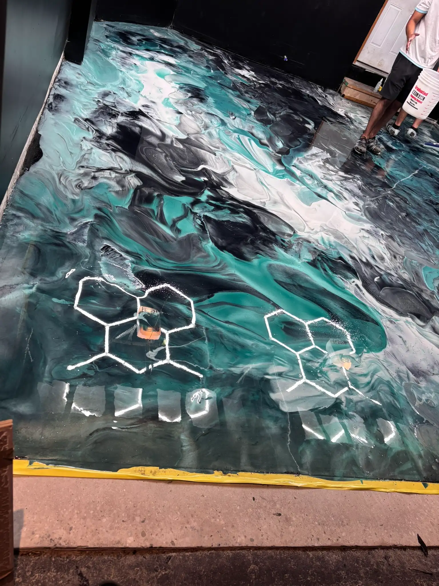 Full garage view of metallic epoxy swirl flooring with person holding epoxy bucket